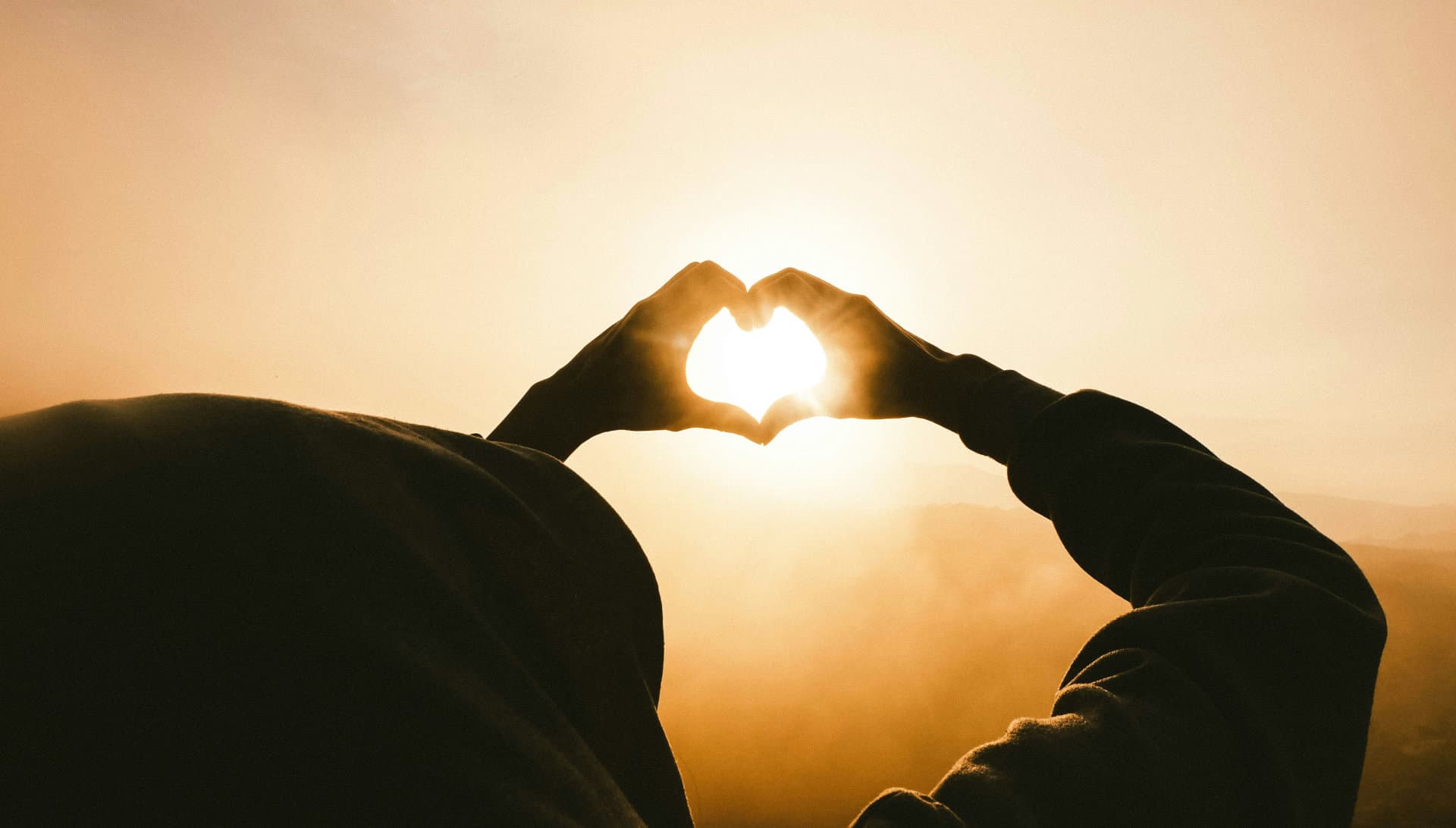 Manos formando un corazón con el sol al fondo, simbolizando energía renovable
