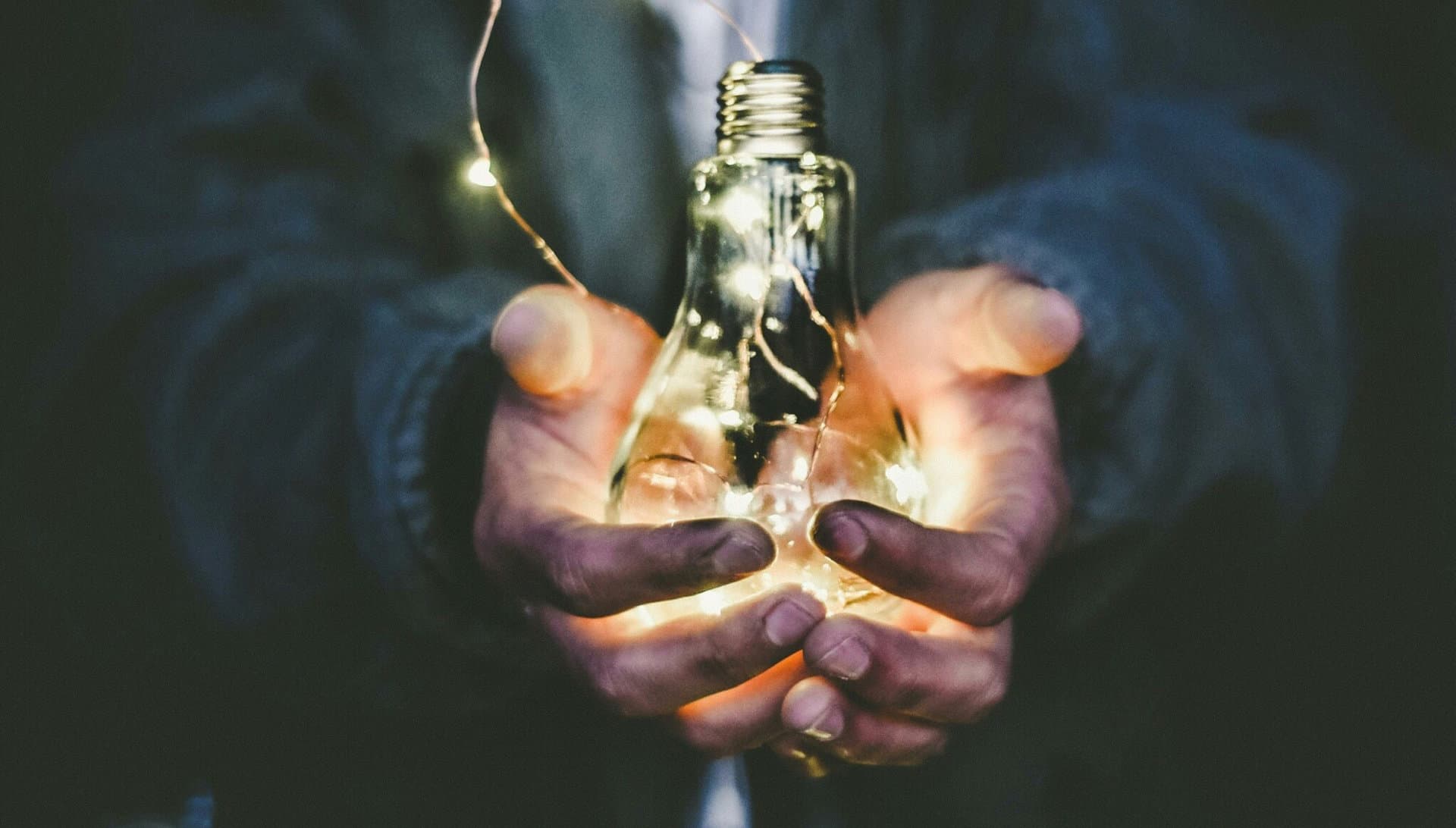 Manos sosteniendo una bombilla con luces LED, representando energía sostenible